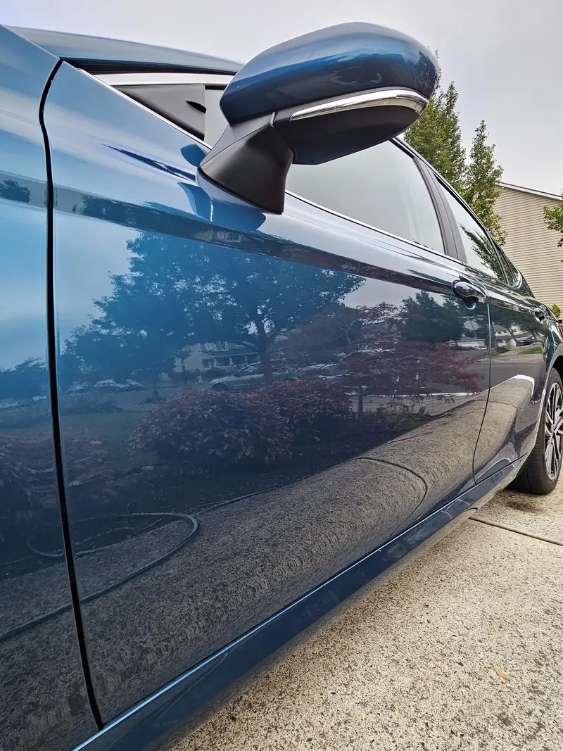 Side and mirror of a blue 2025 Toyota Camry reflecting the street after a hand wash